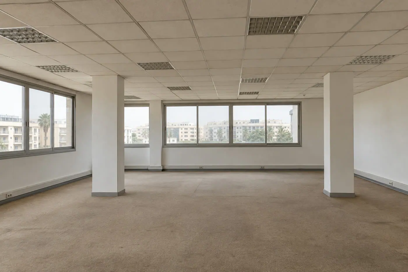 Plateau de bureaux avant travaux : faux plafond nu, sol brut, poteaux apparents
